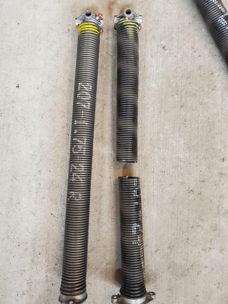 Intact and broken torsion springs on concrete — why a garage door will not close