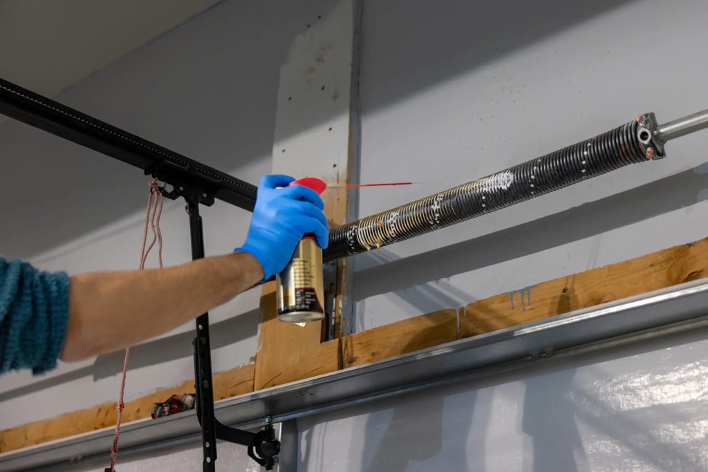 Technician lubricating a garage door torsion spring during a tune-up — Ottawa