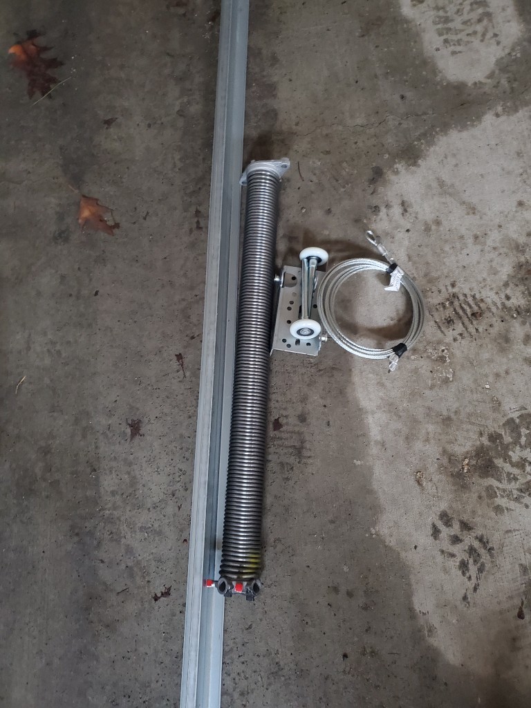 Extension spring, cable, roller bracket, and track laid out for garage door replacement — Ottawa